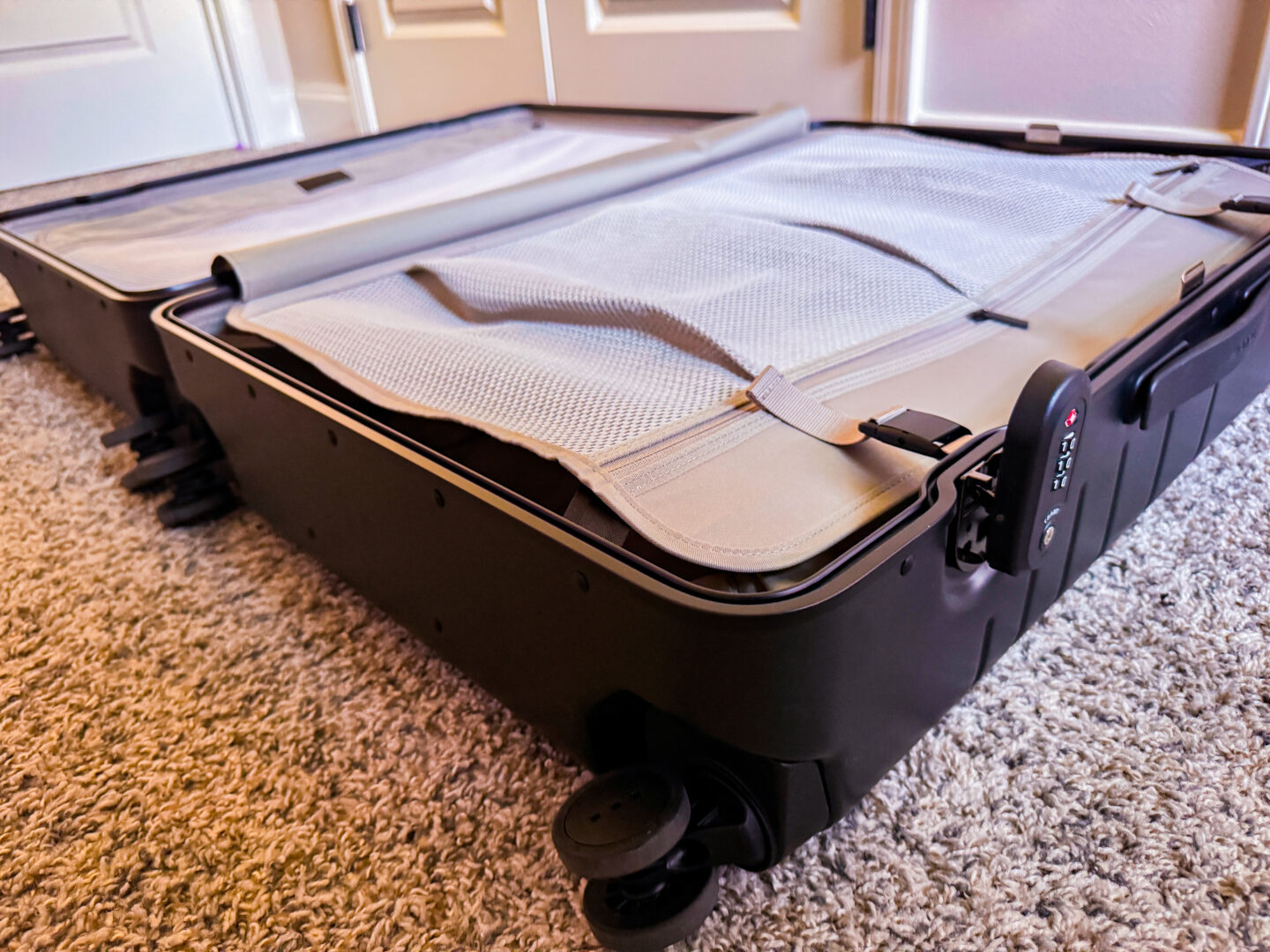 Inside the Monos Hybrid Check-In Large - has two compartments, one with a full interior zippered compartment and one with clips no exterior zippers on a carpeted floor